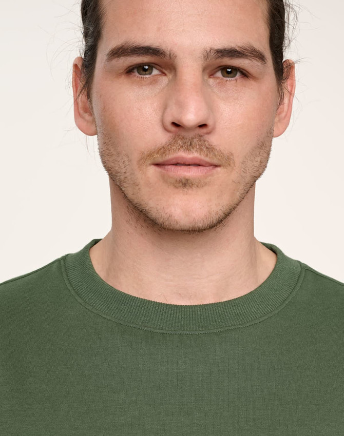 A close-up of a person wearing a green unisex crew neck sweater with a logo on the chest.