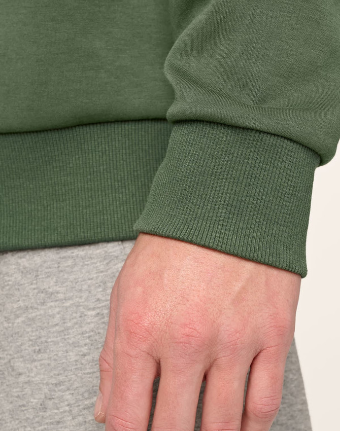 A close-up of a hand wearing a green unisex crew neck sweater, showcasing the ribbed cuff detail.
