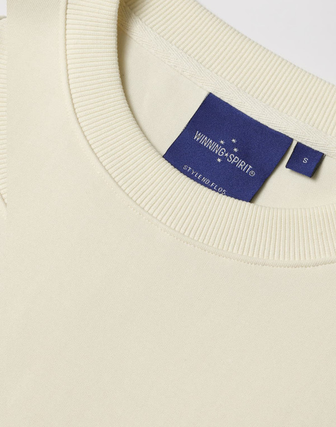 A cream unisex crew neck sweater featuring a ribbed collar and a brand tag.