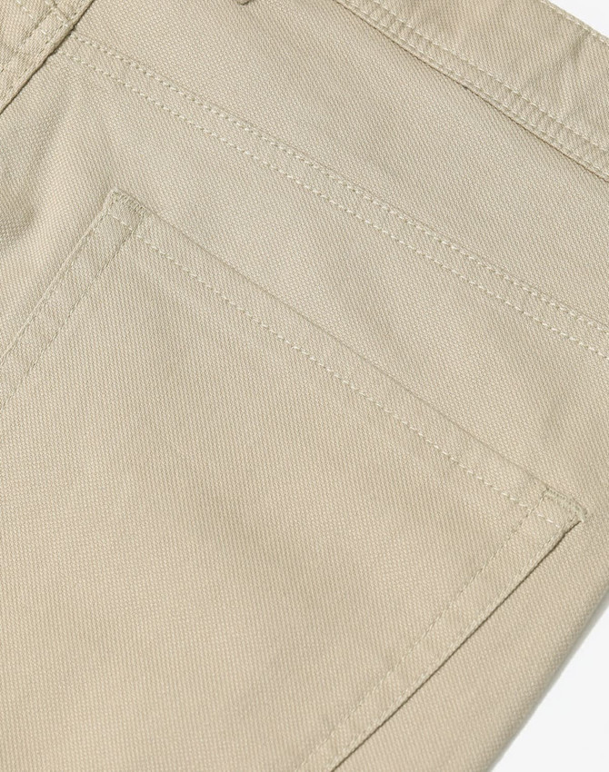 A close-up of beige chino pants, featuring a pocket and textured fabric details. The pants have a logo on them.