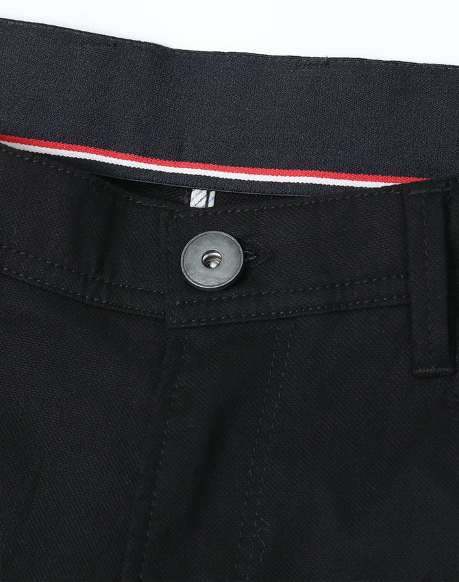 A close-up of black chino pants featuring a button and detailed waistband with a contrasting stripe.