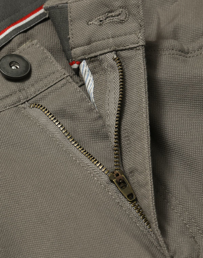 A close-up of grey chino pants showcasing a zippered fly and button closure, with a hint of contrasting interior detail.