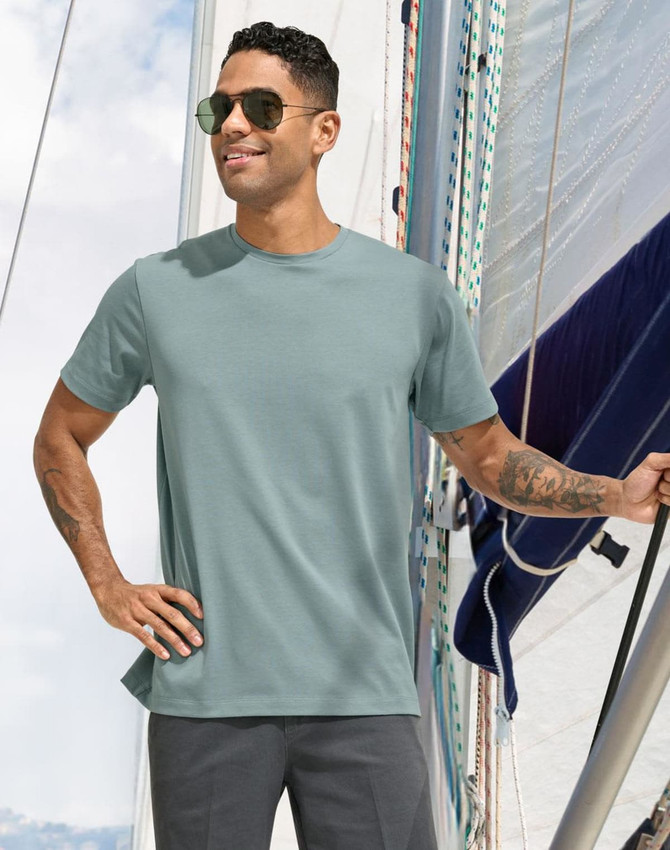 Men's premium cotton short sleeve T-shirt in a soft green shade, featuring a logo, worn by a man on a sailboat.