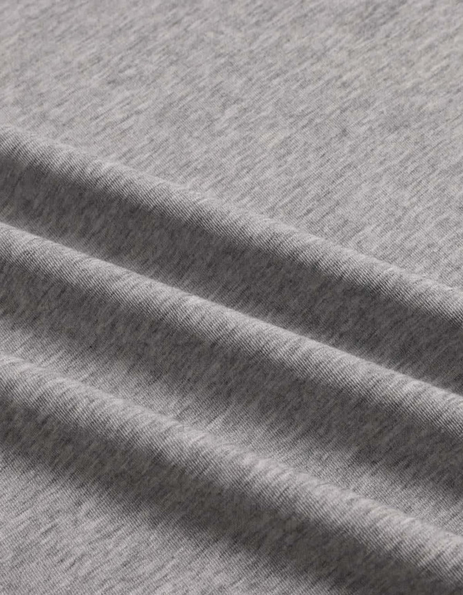 A close-up of a grey premium cotton T-shirt fabric, featuring a soft, textured finish and gentle folds.