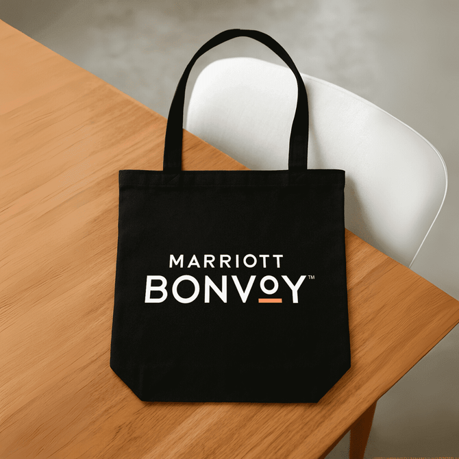 A black tote bag with handles, featuring a logo on the front, placed on a wooden table.