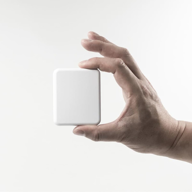 A hand holding a compact, square, white power bank with a sleek design and a soft finish.