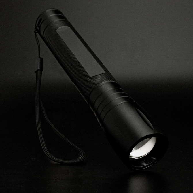 A Swiss Peak 10W Cree Torch features a sleek black design with a textured grip and a wrist strap for easy handling.