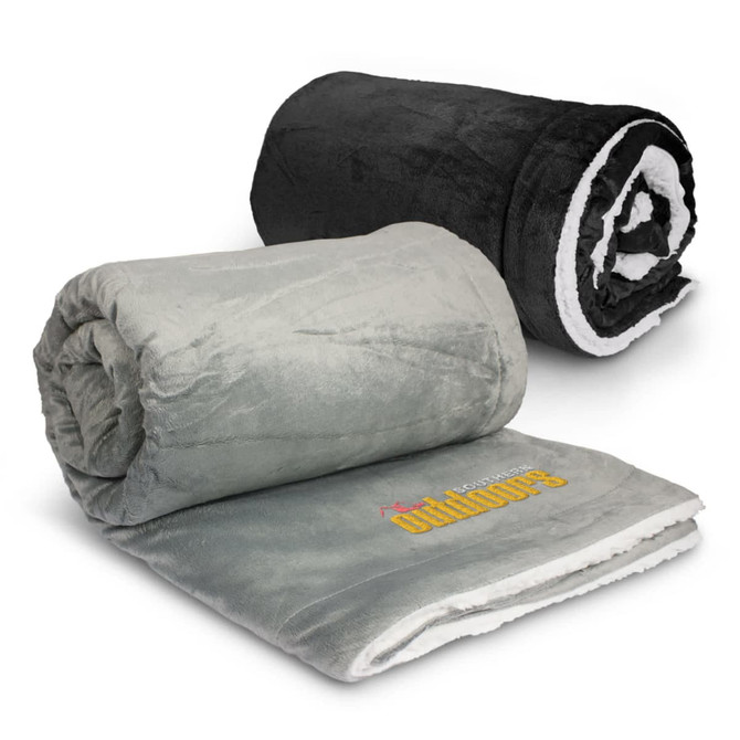 Two rolled luxury blankets are displayed; one is black and the other is light green with a white underside. Each blanket features a logo.