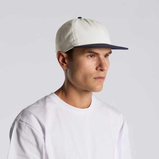 A cap featuring a two-tone design with a light-coloured crown and a navy peak, worn by a model.