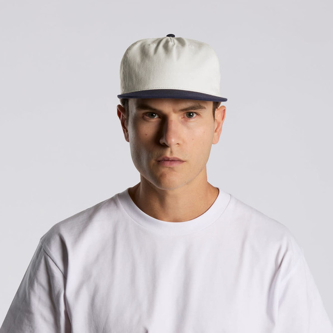 A two-tone cap featuring a cream body and navy peak, displayed on a model wearing a white t-shirt.