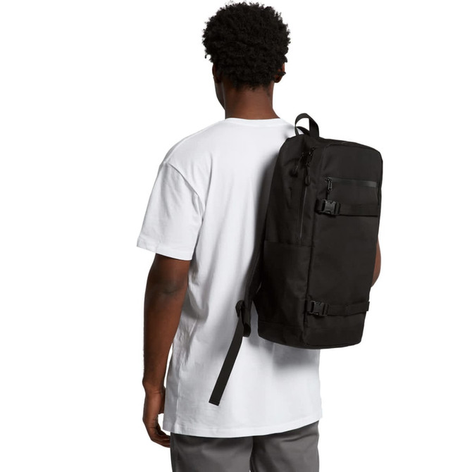 A man in a white t-shirt carries a black recycled strap backpack on his back, featuring multiple compartments and a logo.