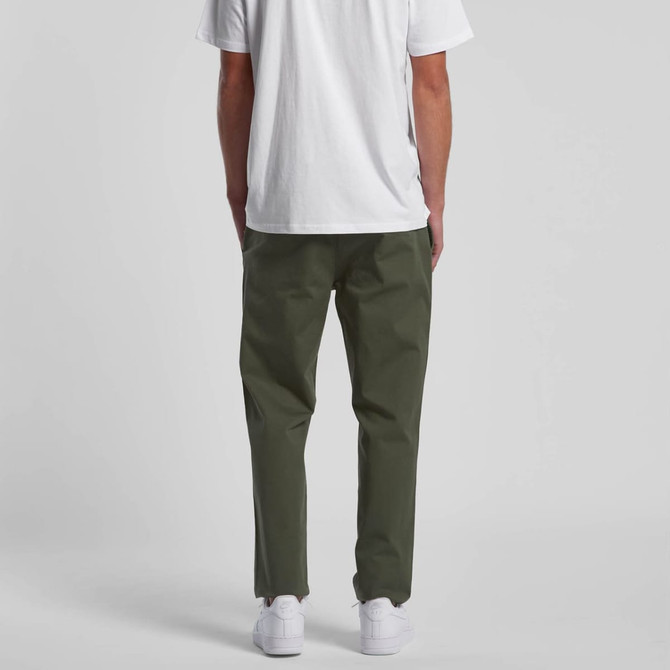 Straight pants in a dark green colour, worn with a plain white t-shirt and white shoes. Features a branding logo.