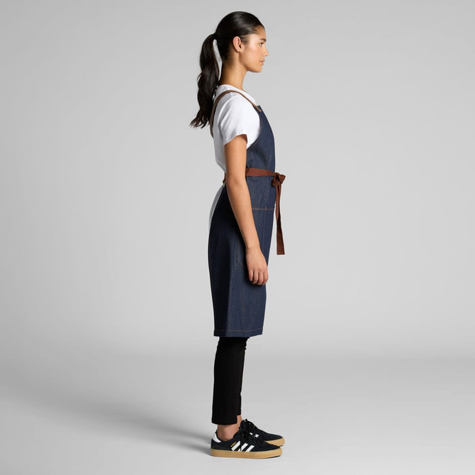 A denim apron in blue with a brown belt, worn by a person in a side profile view.