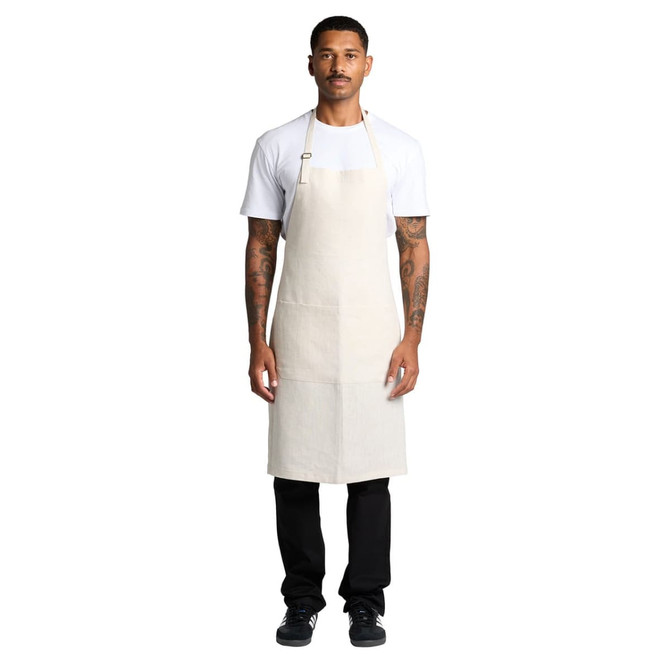 A man wearing a beige linen apron over a white t-shirt and black pants, featuring a logo.