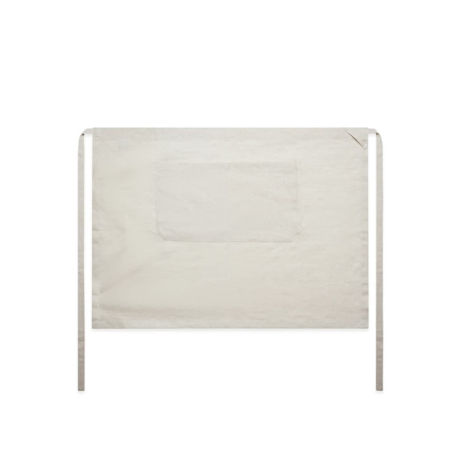A linen half apron in a light beige colour with ties and a front pocket. The design is simple and functional.