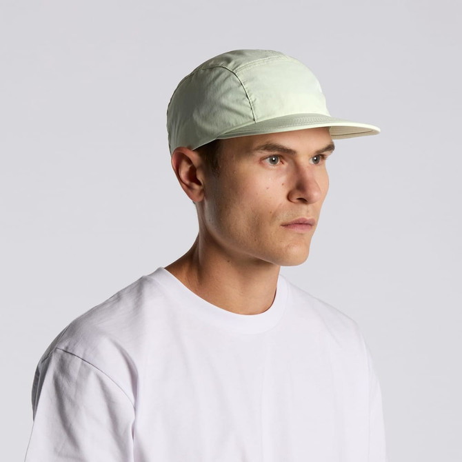 A light green nylon cap with a stiff brim, worn by a model against a plain background.