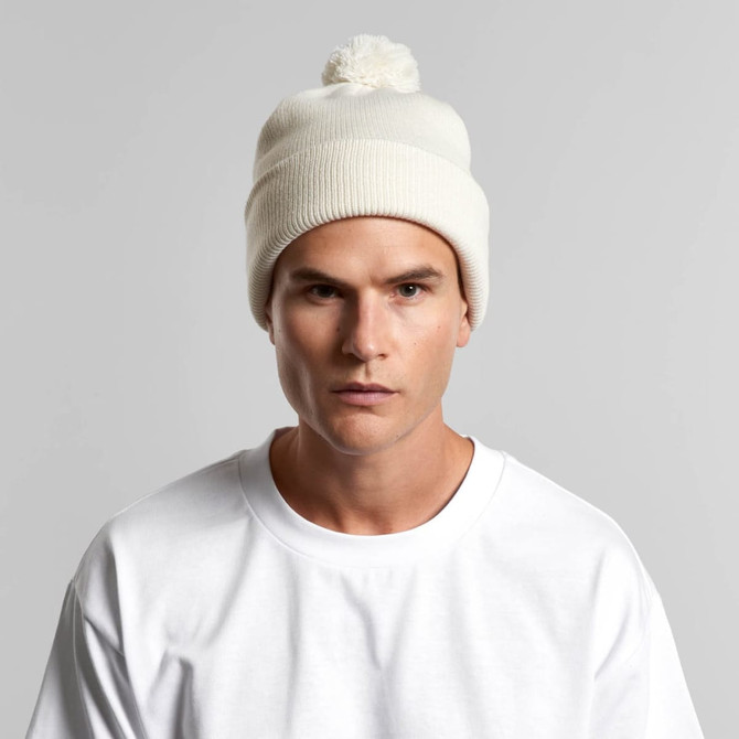A cream Pom Pom Beanie worn by a model, featuring a fluffy top pom and a ribbed design.