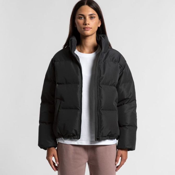 A puffer jacket in black, featuring a zip-up front and a casual, oversized fit. The model wears a white top underneath.