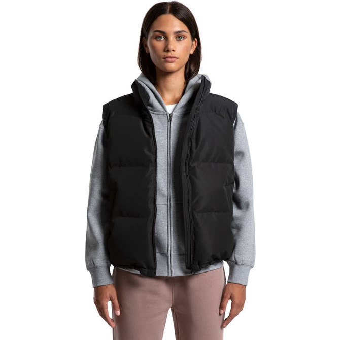 A woman wearing a black puffer vest over a grey hoodie, with a minimalist design and a logo on the vest.