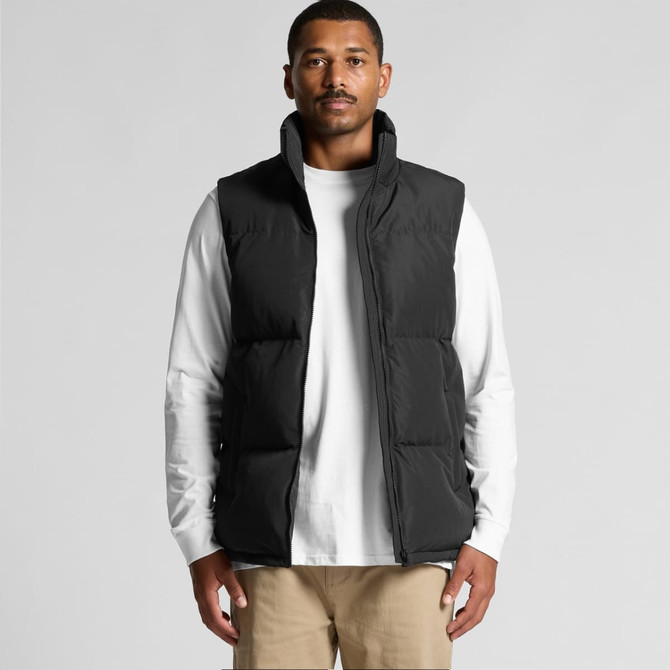 A black puffer vest worn by a man over a white long-sleeve shirt, featuring a logo on the front.