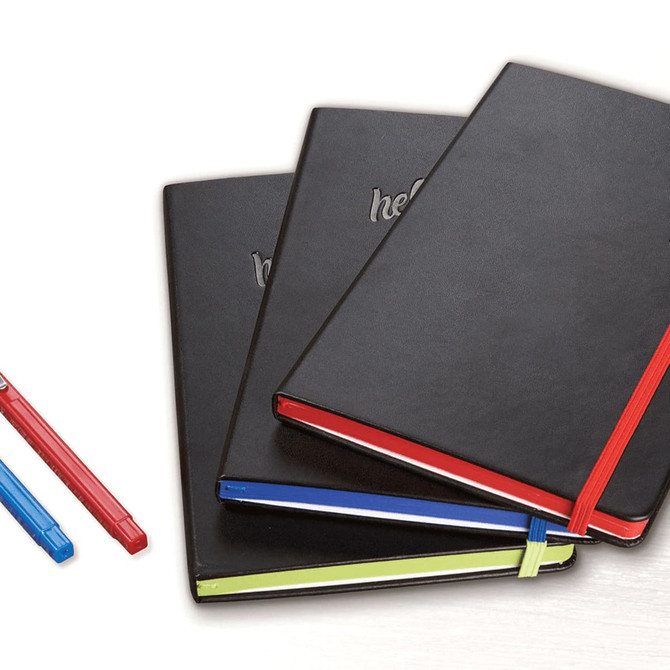 A set of three black bound journals with coloured elastic bands and pens in blue, red, and green.