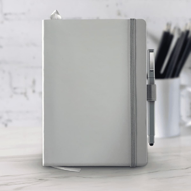 A grey hard-bound journal with an elastic closure and a pen attached, set against a blurred background of stationery.