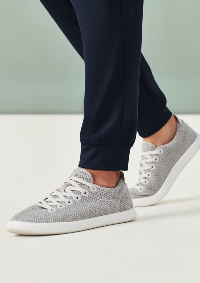 A pair of women's jogger scrub pants in navy, complemented by grey sneakers, featuring a logo on the sneakers.