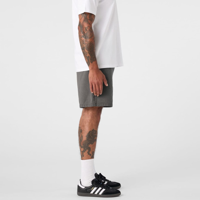 A person stands in profile wearing faded grey dress shorts and a white t-shirt, paired with black shoes and socks.