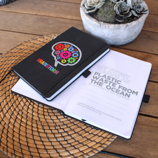 A black notebook with a colourful gear design, open to display its pages. It features a branding logo and a textured cover.