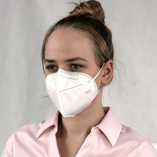 A white N95 respirator face mask is worn by a woman with a casual hairstyle, against a light background.