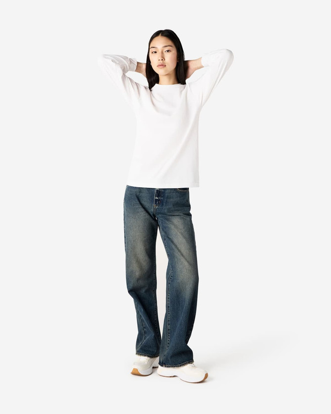 A model wearing a white heavyweight cotton unisex long sleeve T-shirt paired with blue jeans and white shoes.