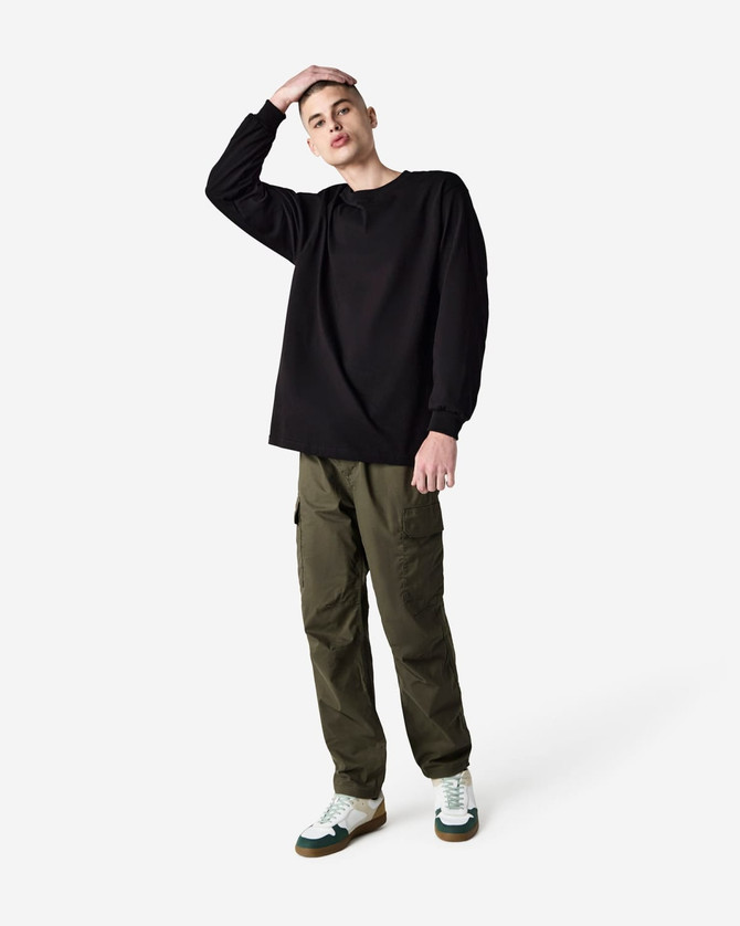 A model wearing a black heavyweight cotton unisex long sleeve T-shirt, paired with green cargo pants and white sneakers.