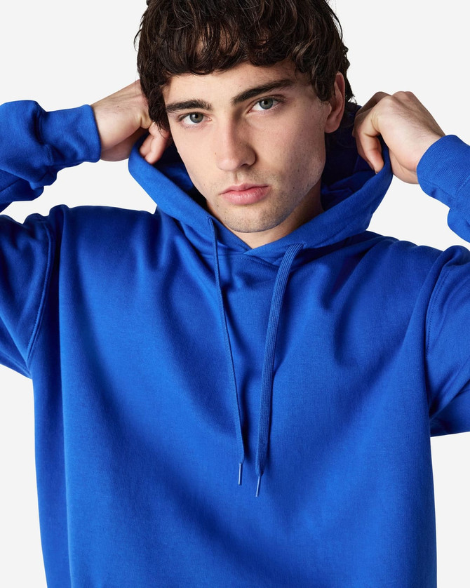 A blue Gildan Softstyle adult hooded sweatshirt worn by a model adjusting the hood. The sweatshirt has a logo.
