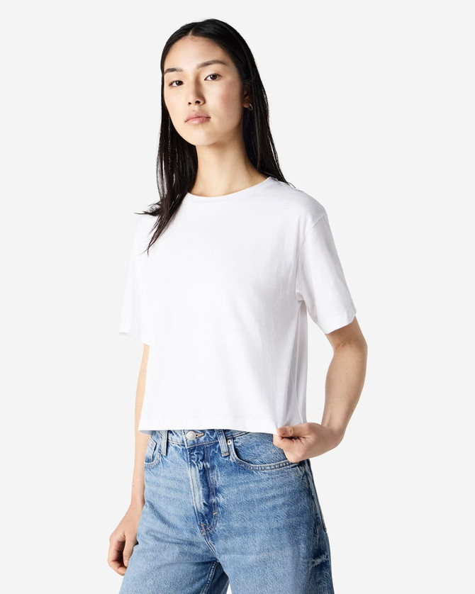 A white women's boxy t-shirt with short sleeves, paired with light blue jeans, featuring a branding logo.