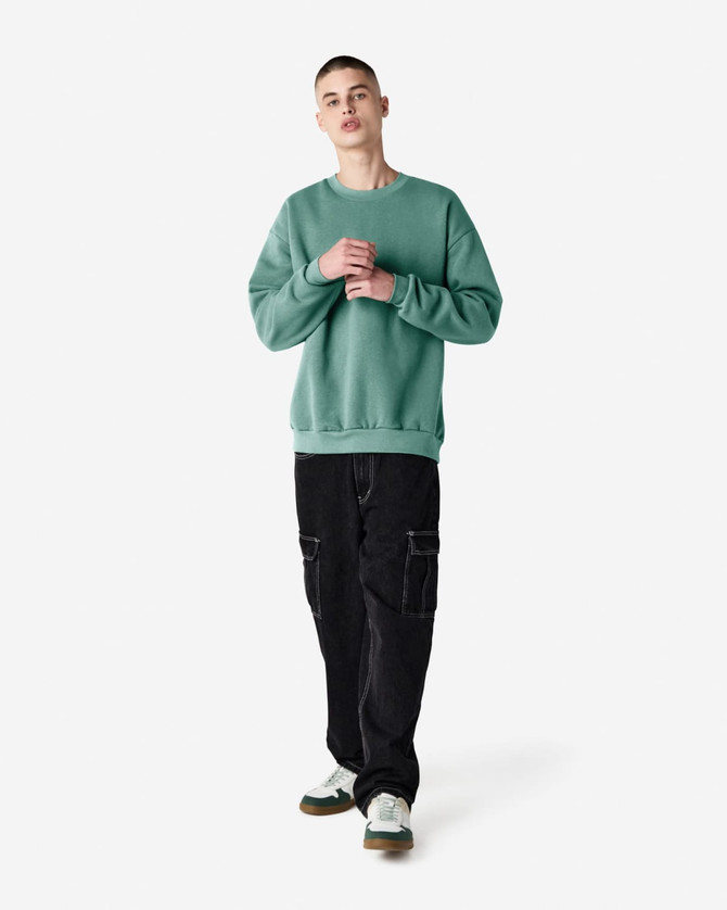 A unisex crewneck sweatshirt in green, paired with black cargo pants, featuring a logo on the front.