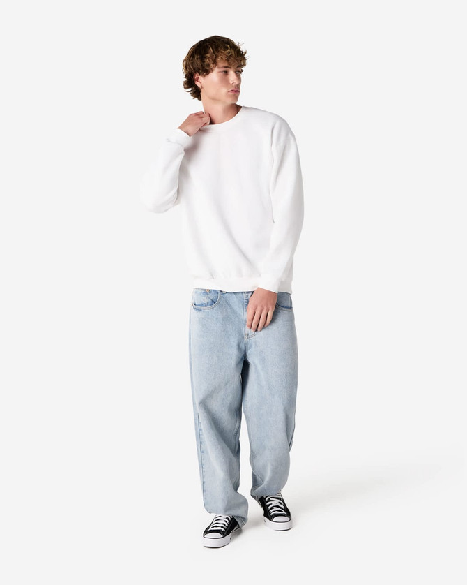 A unisex crewneck sweatshirt in white, paired with light blue baggy jeans, worn by a model. Features a branding logo.