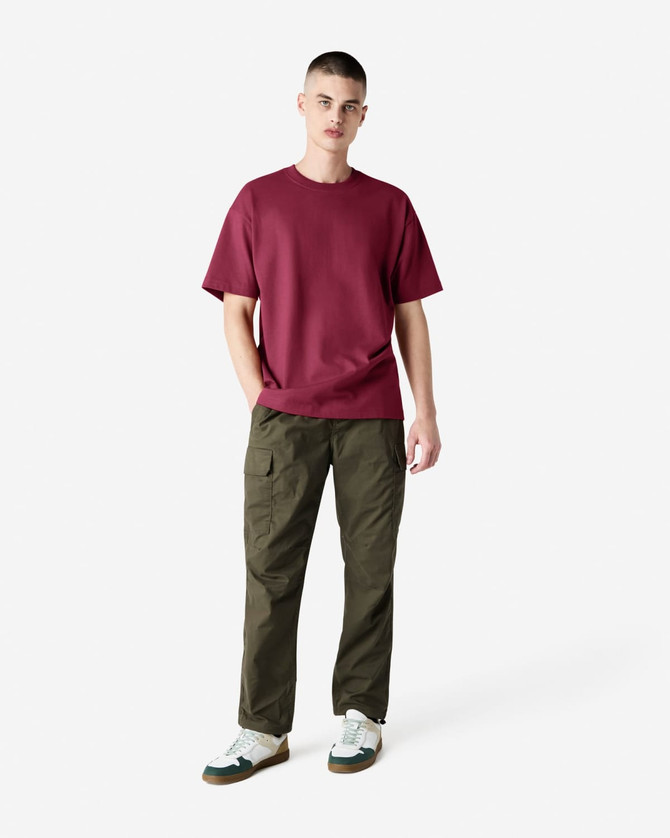 A model wearing a maroon heavyweight T-shirt and olive green cargo pants, featuring a logo.