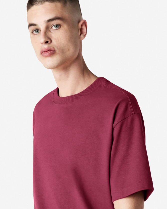 A maroon American Apparel Super Heavyweight T-Shirt displayed on a model with short hair and a neutral background.