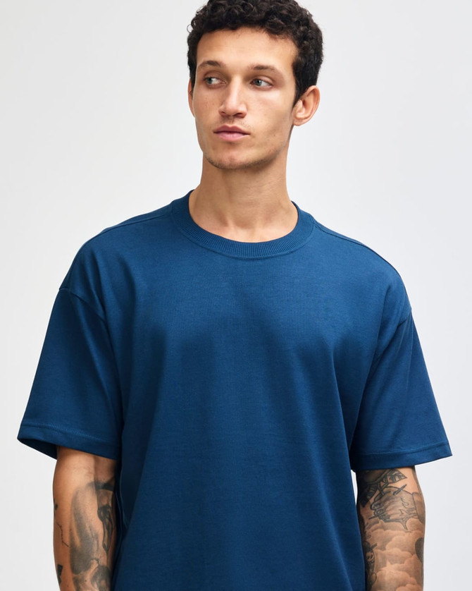 A model wearing a teal American Apparel Super Heavyweight T-Shirt, featuring a round neckline and short sleeves.
