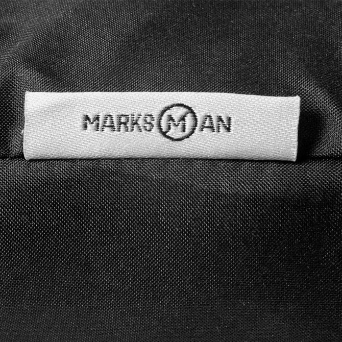 A close-up of a black fabric with a branded tag featuring the name "Marksman" stitched on it.
