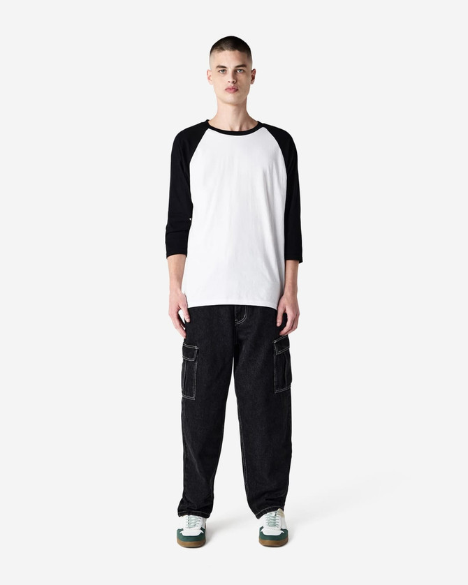 A unisex raglan T-shirt in white with black sleeves, paired with dark cargo pants. The model stands against a plain background.