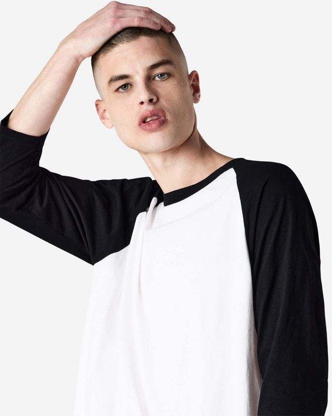 A unisex raglan T-shirt featuring black sleeves and a white body, worn by a model with a shaved head.