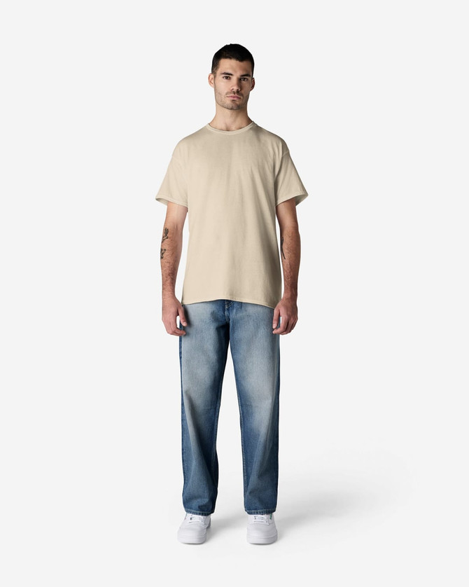 A light beige Gildan Light Cotton T-Shirt paired with faded blue jeans and white shoes, featuring a branding logo.