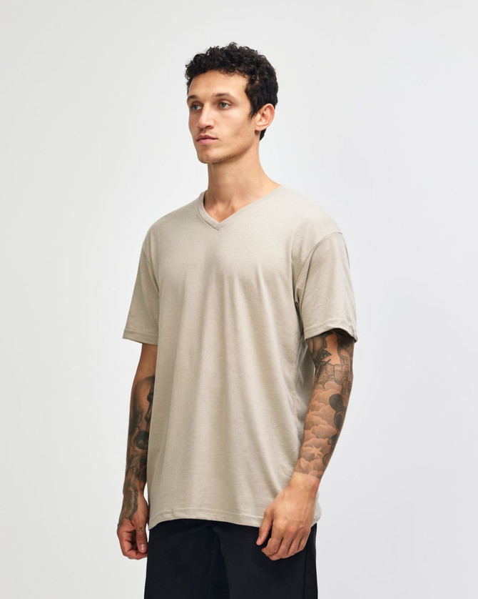 A unisex V-neck T-shirt in a beige colour, displayed on a model from the side. The shirt has a logo.