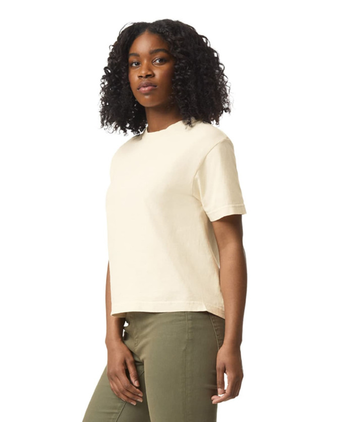 A light beige boxy t-shirt with short sleeves, modelled by a woman with curly hair, featuring a logo.