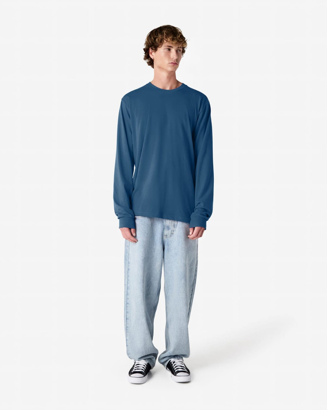 A person wearing a blue long sleeve T-shirt with a relaxed fit, paired with light blue jeans and black shoes.
