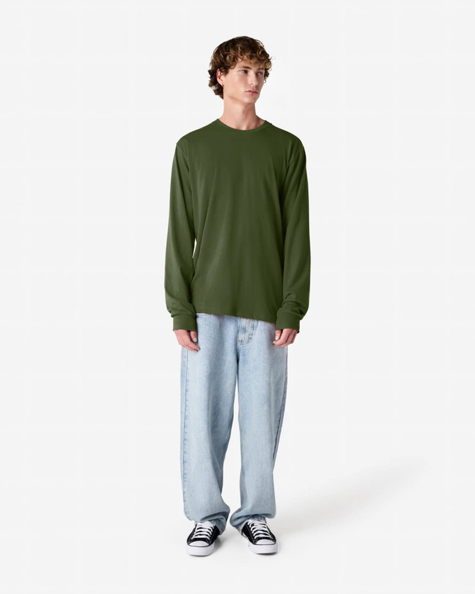 A long sleeve t-shirt in olive green, displayed on a model wearing loose-fitting light denim jeans and black sneakers.