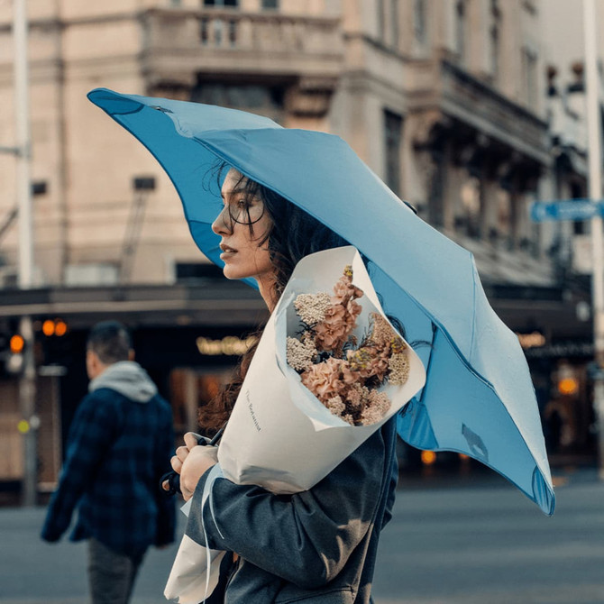 A blue umbrella held by a woman, who is also carrying a bouquet of flowers, in an urban setting.