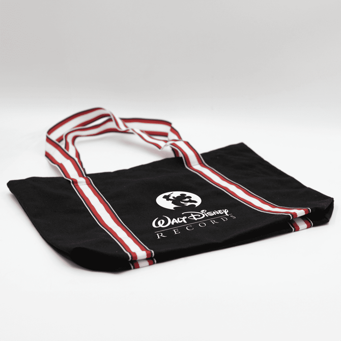 A black canvas tote bag with red and white striped handles and a logo.
