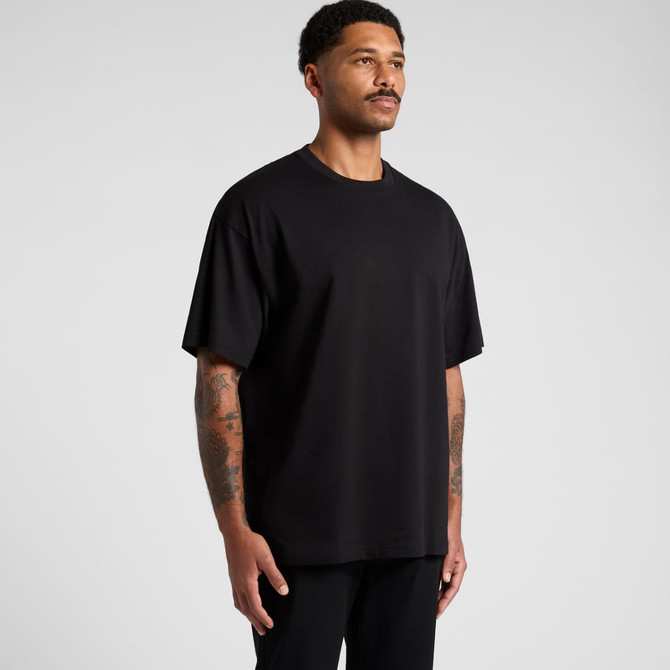 A man stands wearing a black oversized tee, displaying a casual look. The shirt has a logo on it.